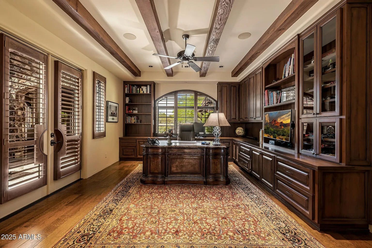Elegant home office with wooden furniture, large desk, bookshelves, and a ceiling fan.