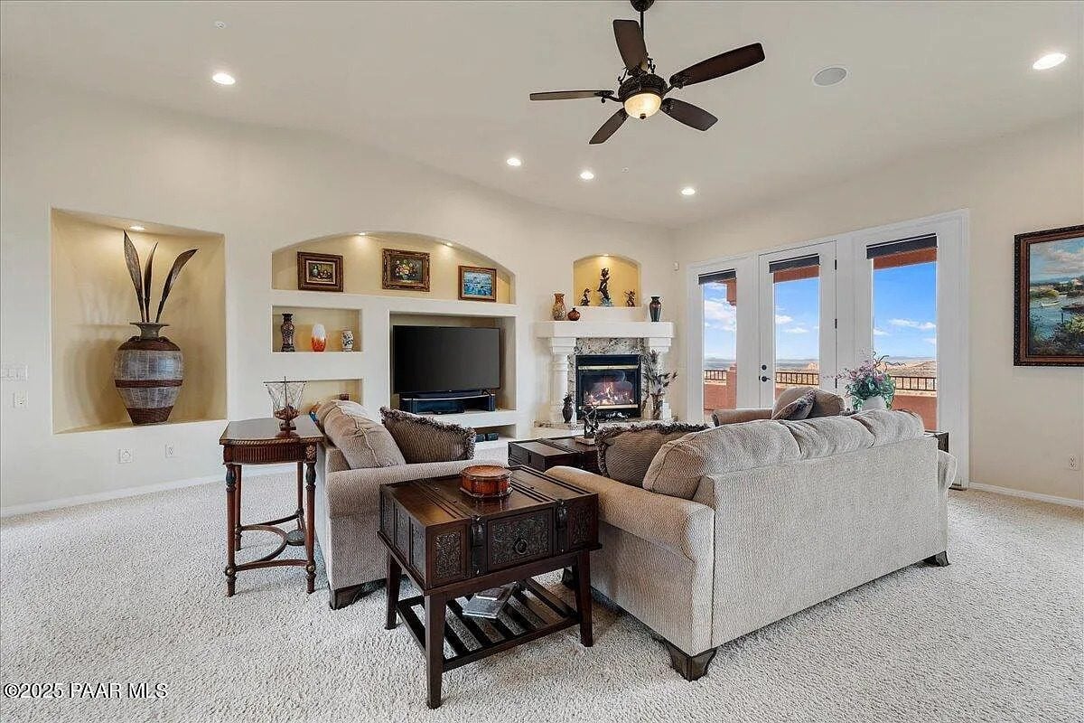Spacious living room with beige sofas, fireplace, TV, ceiling fan, and large windows with a view.