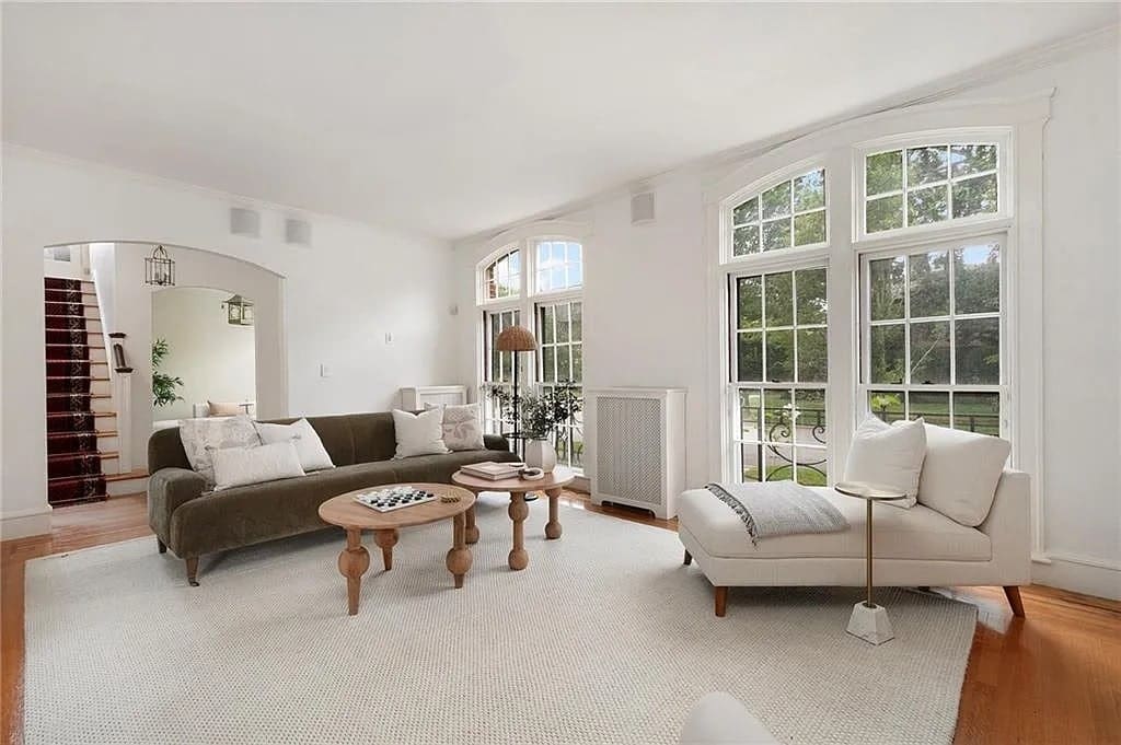 Bright living room with large windows, neutral furniture, and a cozy seating area on a light rug.