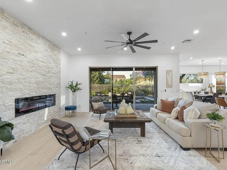 Modern living room with stone fireplace, large windows, beige sofa, and wooden coffee table.
