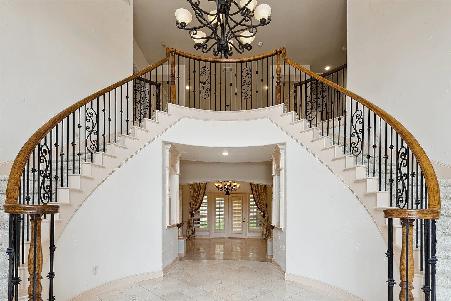 Elegant curved staircase with wrought iron railings and chandelier in a spacious foyer.