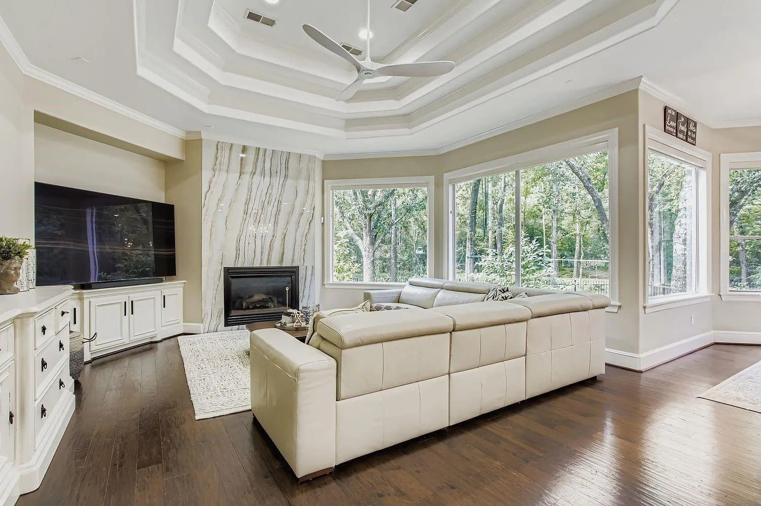 Spacious living room with large windows, white sectional sofa, TV, and fireplace.