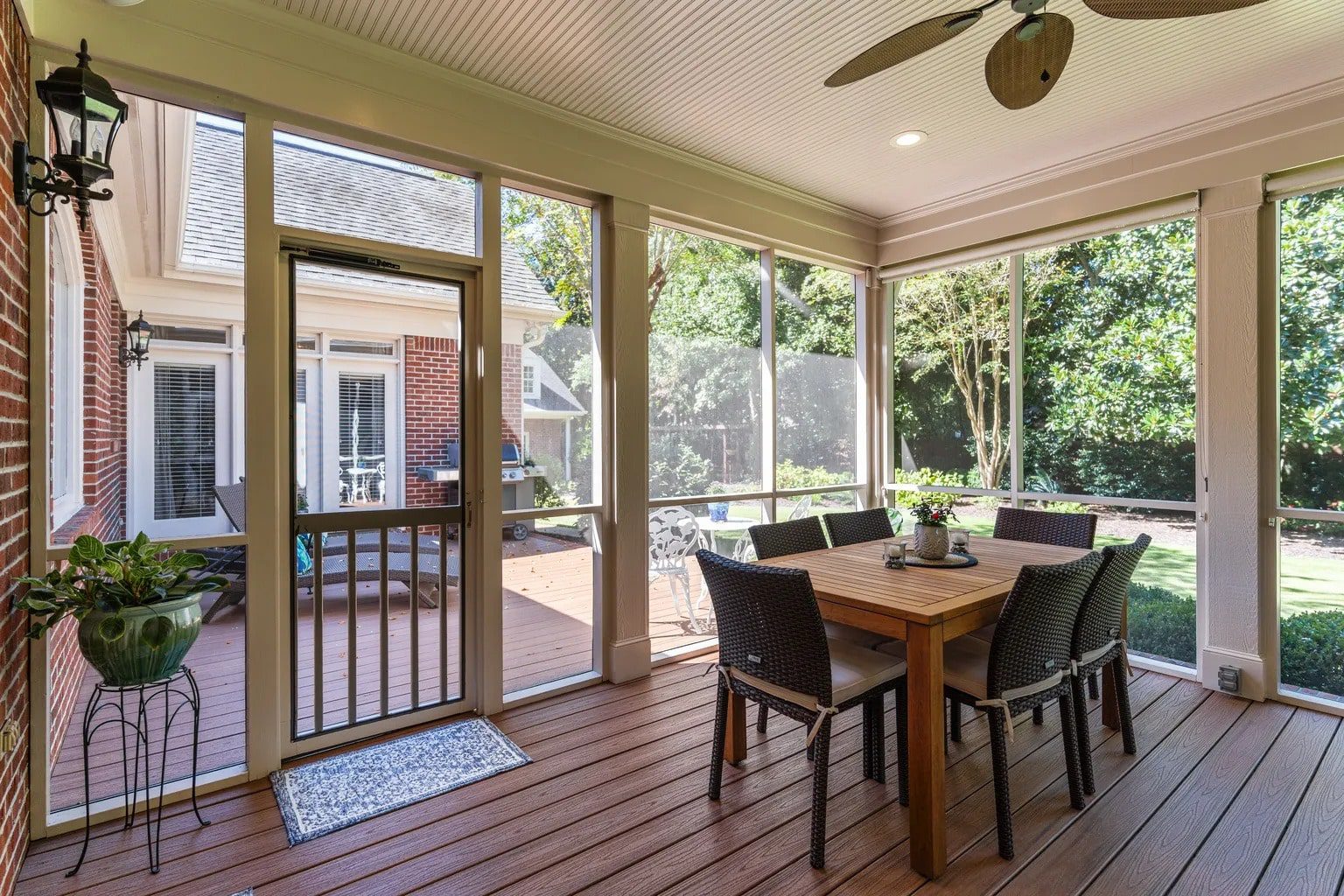 Screened-in porch with a wooden dining table, chairs, and view of a backyard garden.