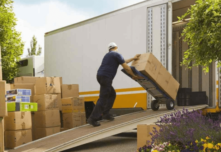 A person pushes a box on a dolly up a ramp into a moving truck.