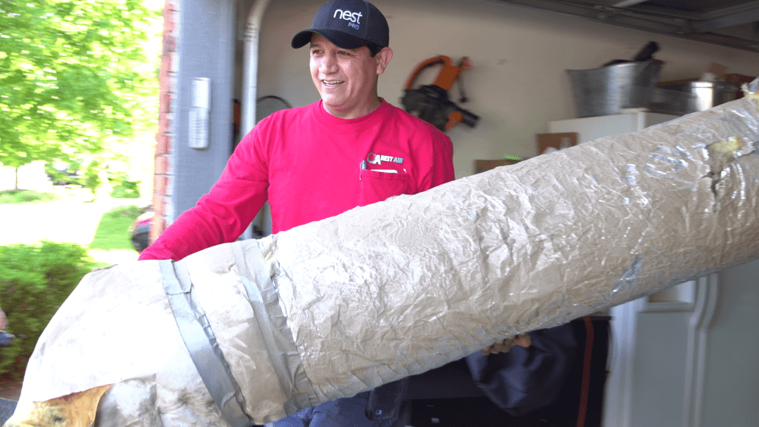 Man in red shirt carrying a large rolled-up carpet out of a garage.