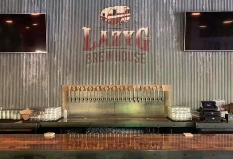 Bar counter with multiple beer taps and 'LazyG Brewhouse' logo on corrugated metal wall.