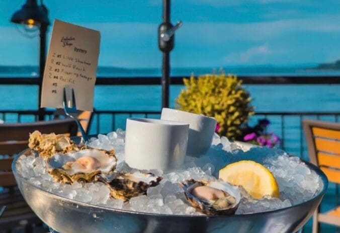 Oysters on ice with lemon wedge, outdoor seating by the water, menu card visible.