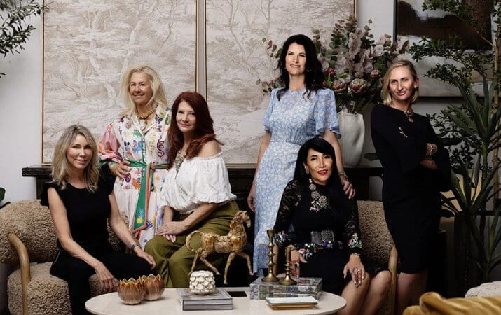 Six women posing together in a stylish, elegant room with art and decor.