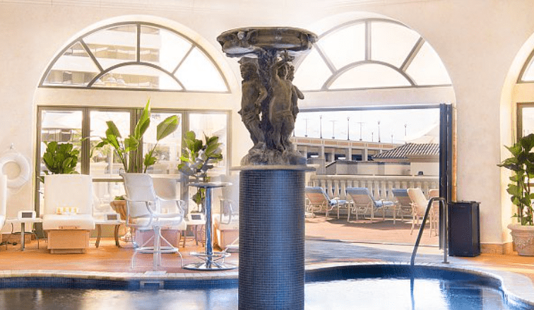 Indoor pool area with a central statue, surrounded by lounge chairs and potted plants.