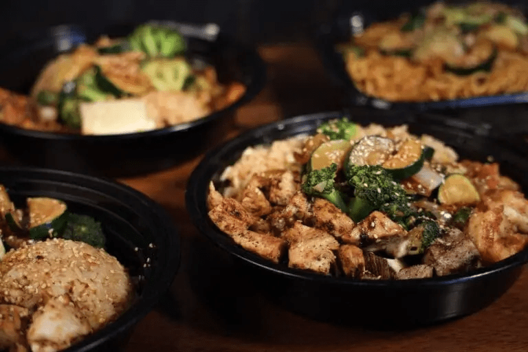 Bowls of grilled chicken, vegetables, and rice on a wooden table.