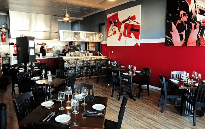 Casual restaurant interior with modern art, set tables, and an open kitchen in the background.