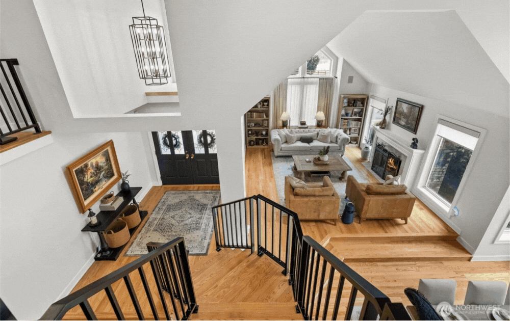 View from staircase of a modern living room with fireplace, sofas, and large windows.