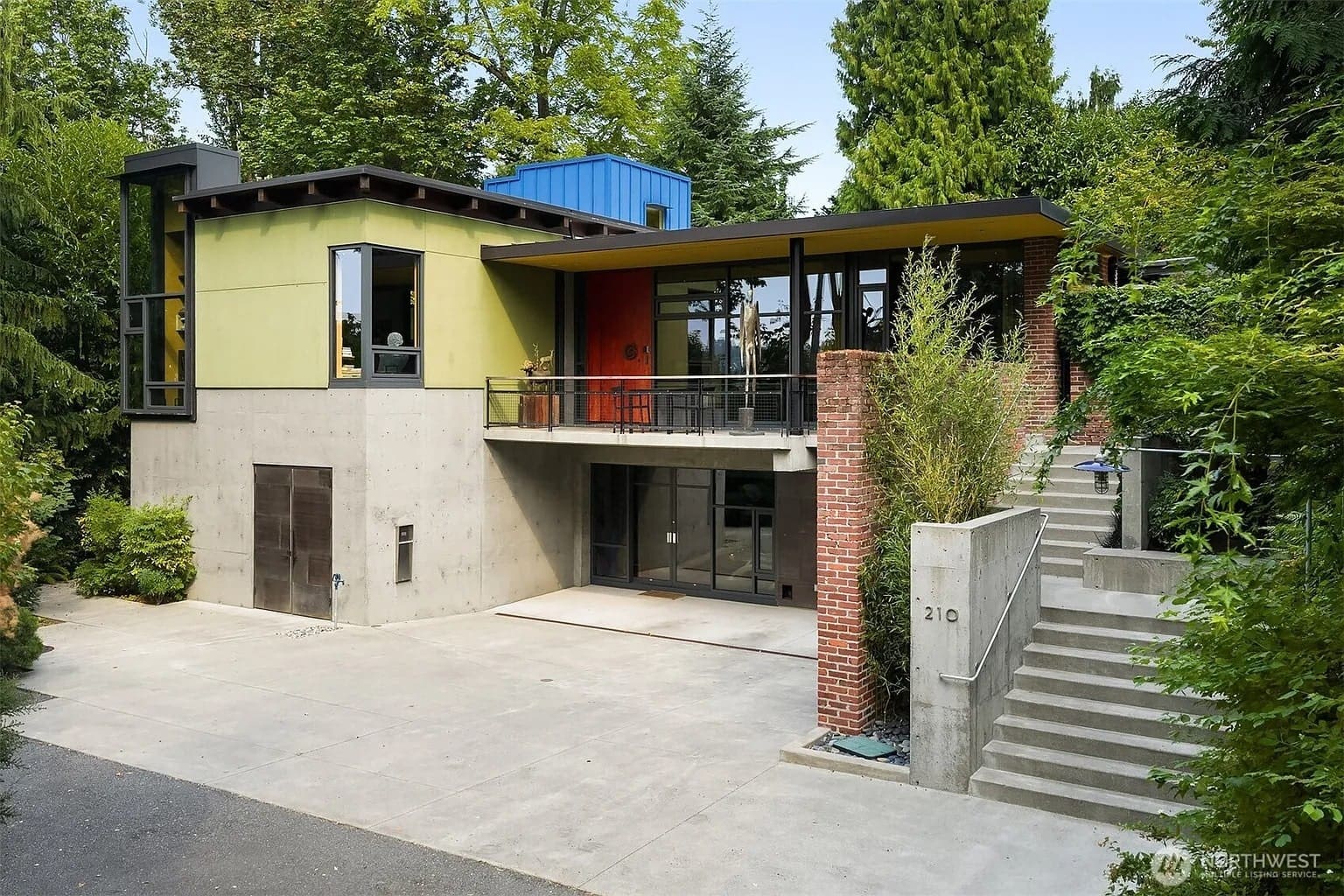 Modern two-story house with colorful facade, large windows, and surrounded by lush greenery.