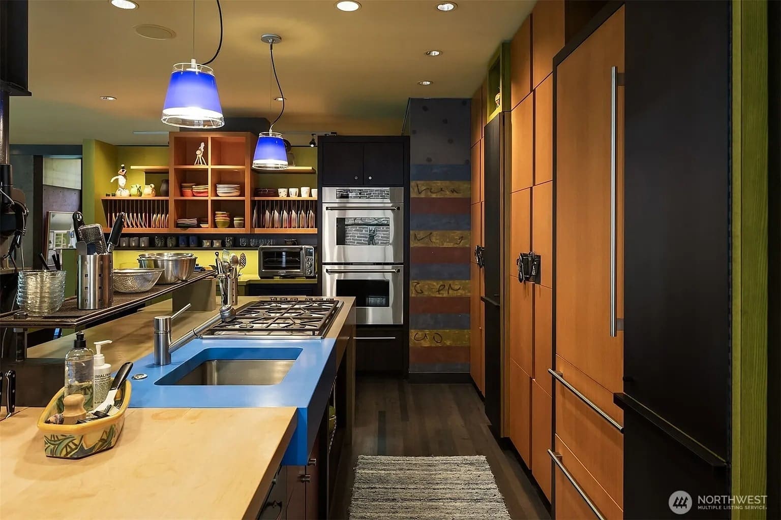 Modern kitchen with blue pendant lights, colorful cabinets, and stainless steel appliances.