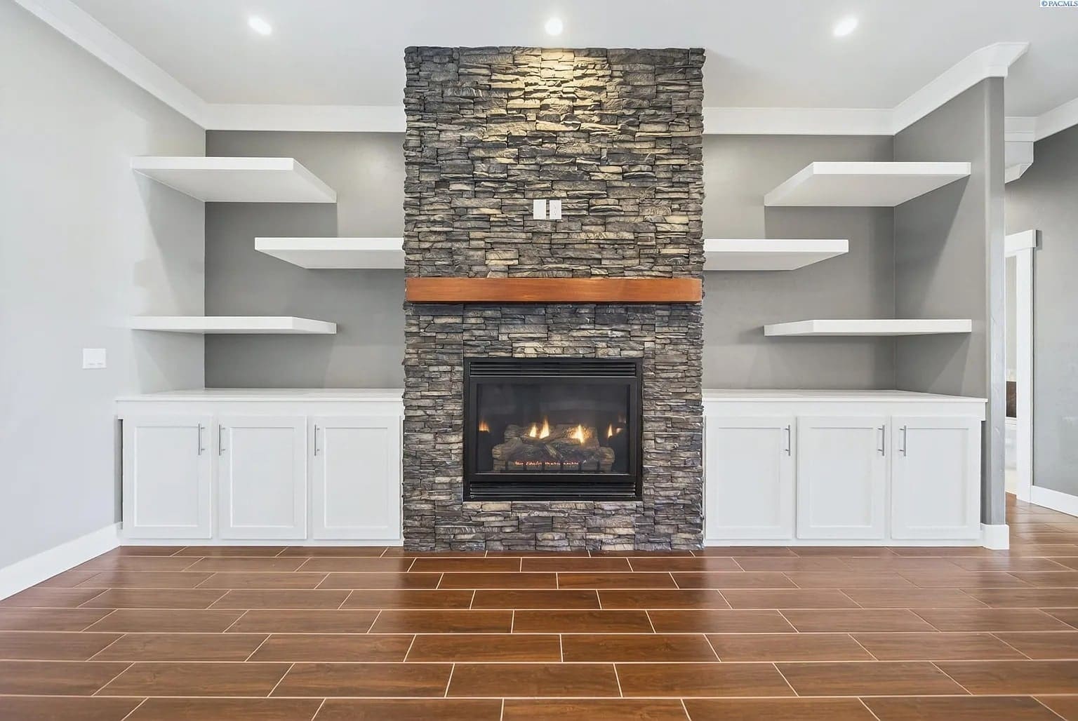 Modern living room with stone fireplace, wooden mantel, white shelves, and cabinets.