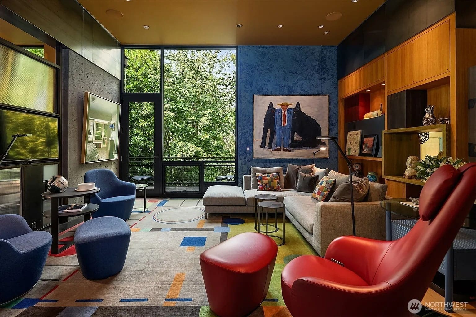 Modern living room with colorful furniture, abstract rug, large windows, and vibrant artwork on the wall.