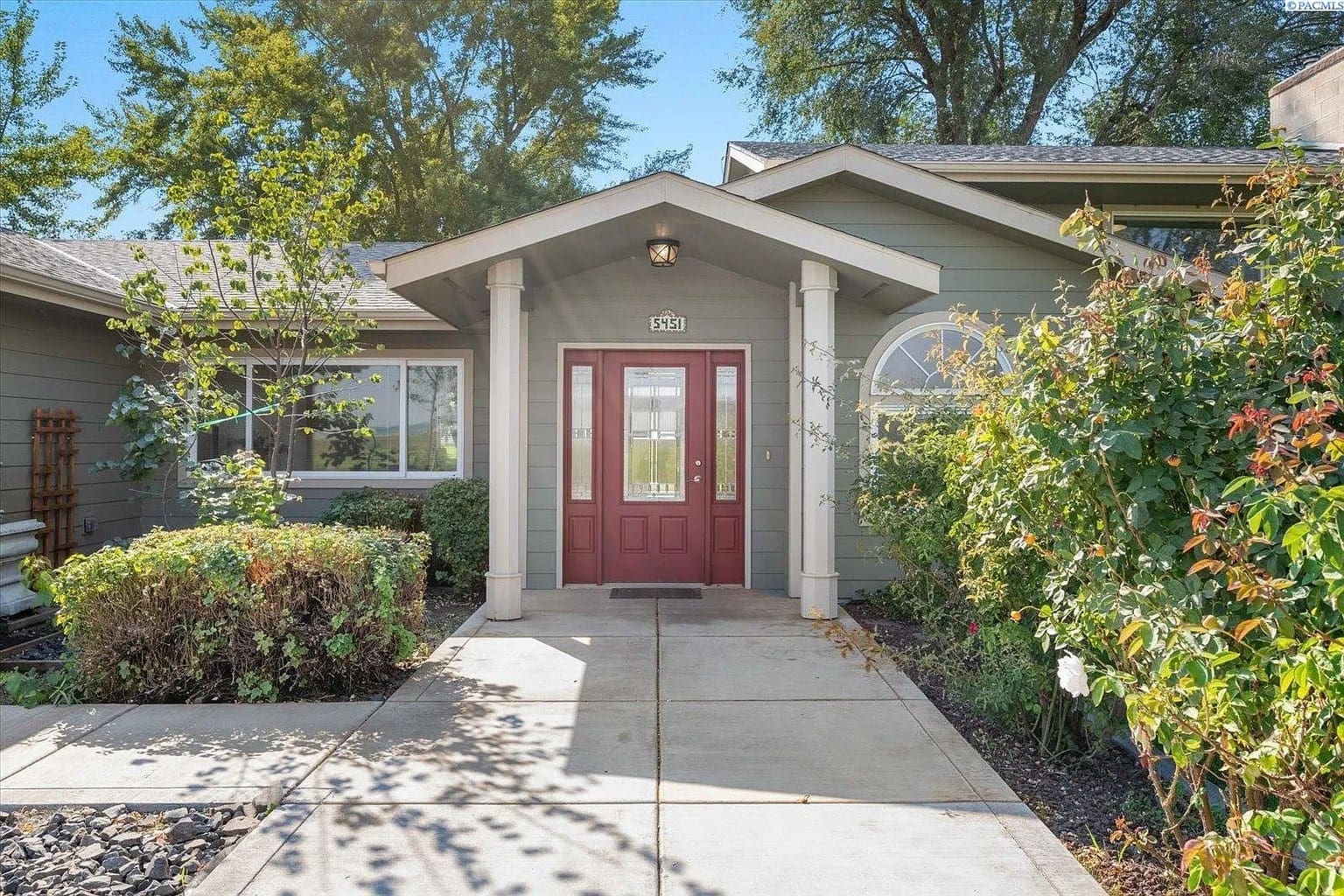 Front view of a house with a red door, surrounded by greenery and a paved walkway.