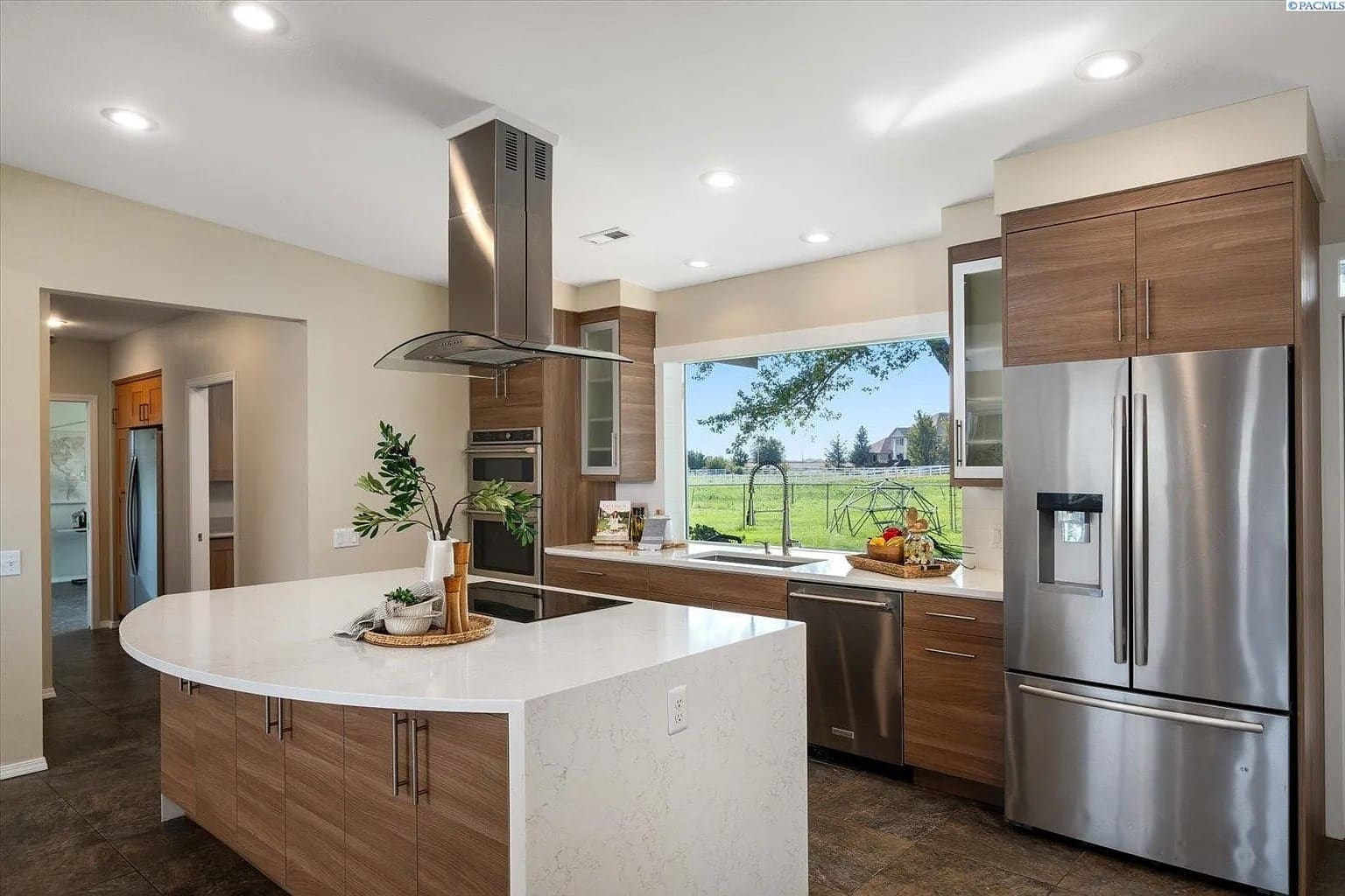 Modern kitchen with stainless steel appliances, large island, and window view of a green field.