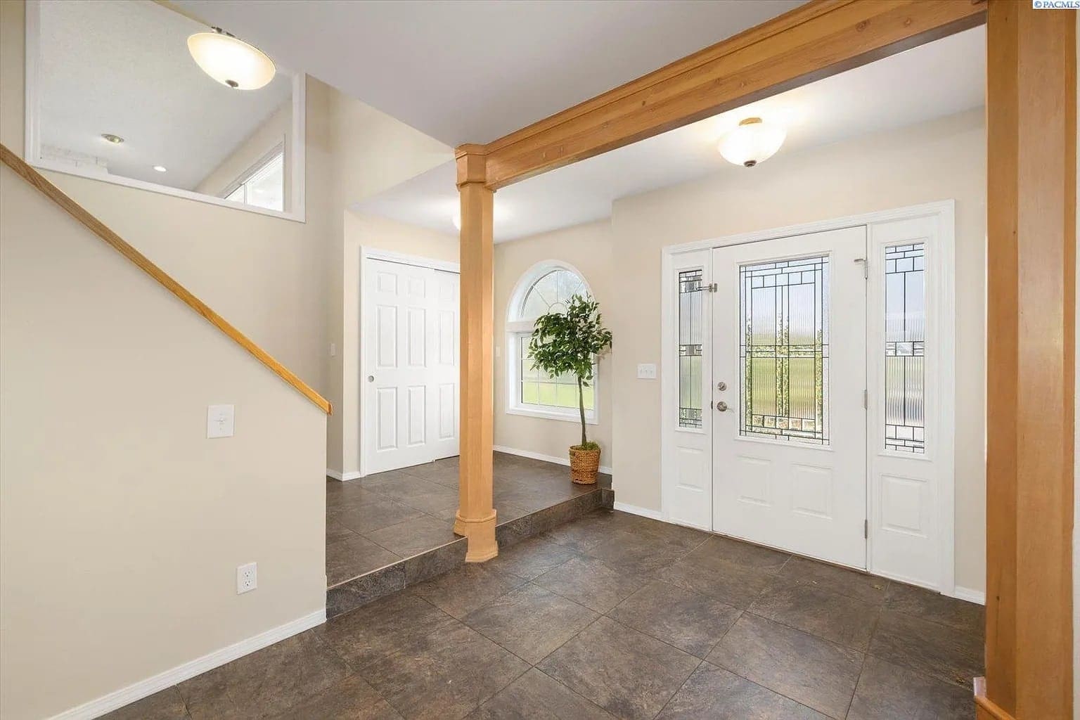 Spacious foyer with tiled floor, wooden columns, potted plant, and decorative glass front door.
