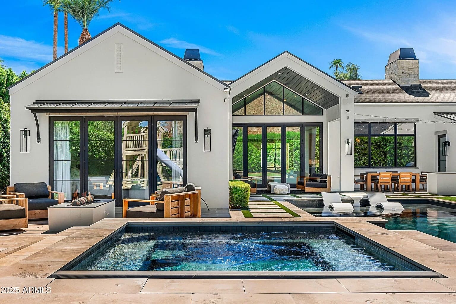 Modern house with large windows, outdoor seating, pool, and spa under a clear blue sky.