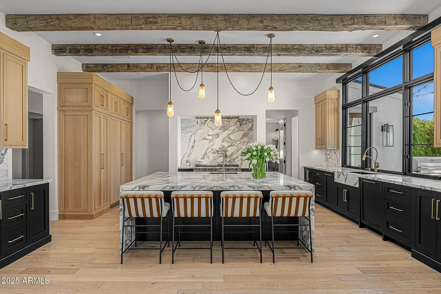 Modern kitchen with marble island, wooden beams, pendant lights, and striped barstools.