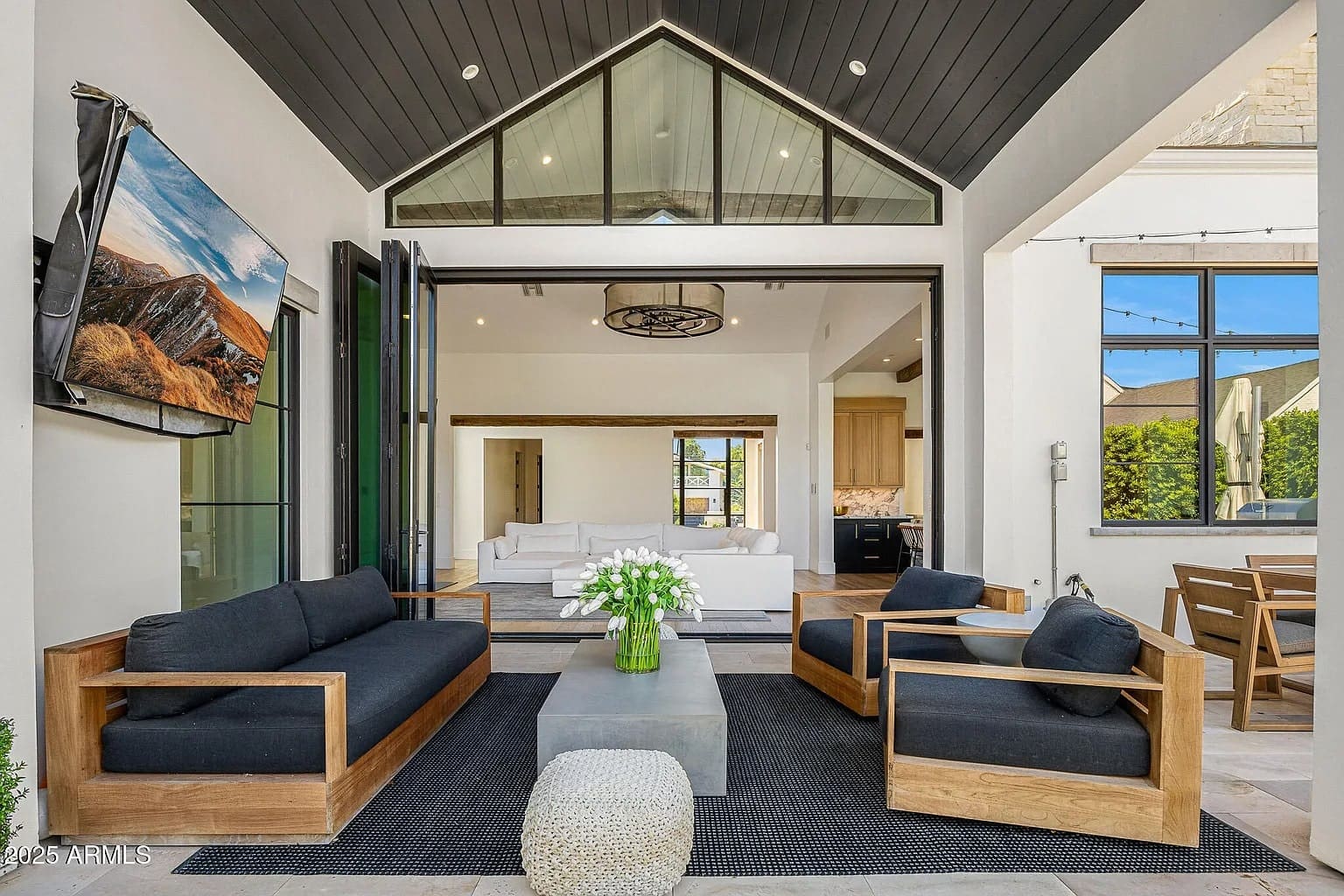 Modern open living space with black and wood furniture, large windows, and a wall-mounted TV.