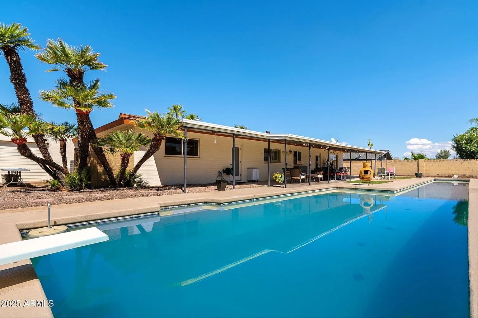 Backyard view of a house with a swimming pool and palm trees under a clear blue sky.