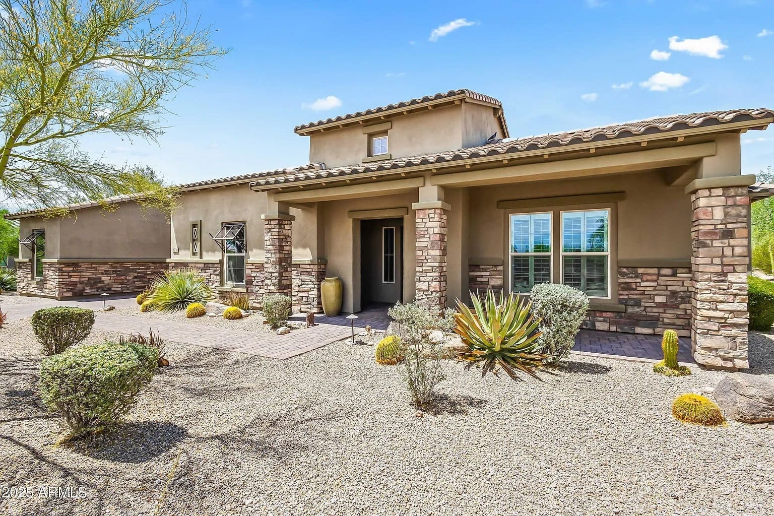 Single-story house with stone accents, desert landscaping, and a clear blue sky.