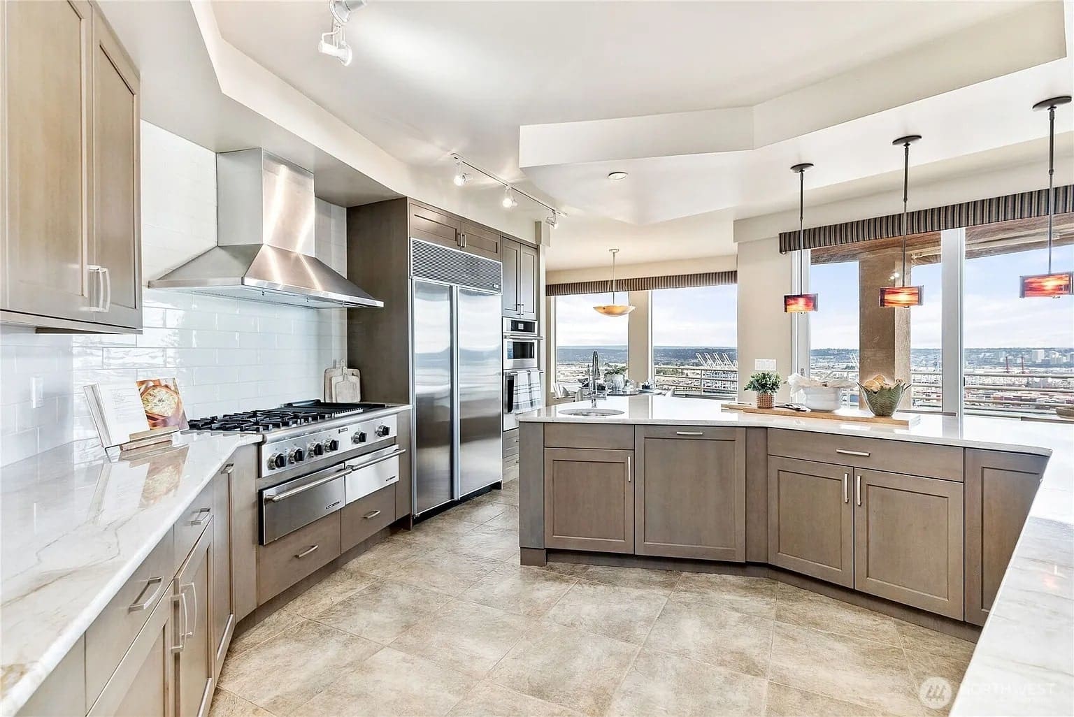 Modern kitchen with stainless steel appliances, marble countertops, and large windows offering city views.