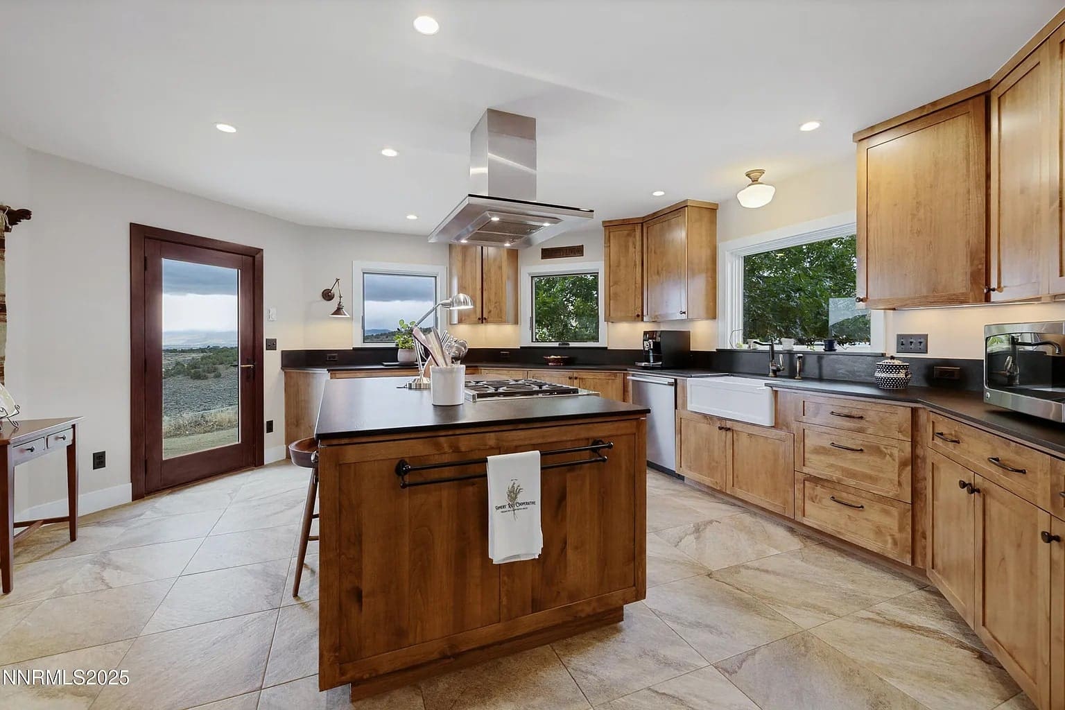 Modern kitchen with wooden cabinets, central island, and large windows overlooking a scenic outdoor view.