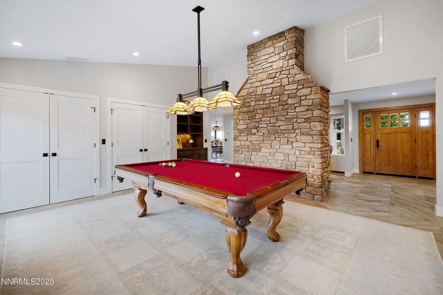 Room with a red pool table, stone fireplace, and wooden doors.