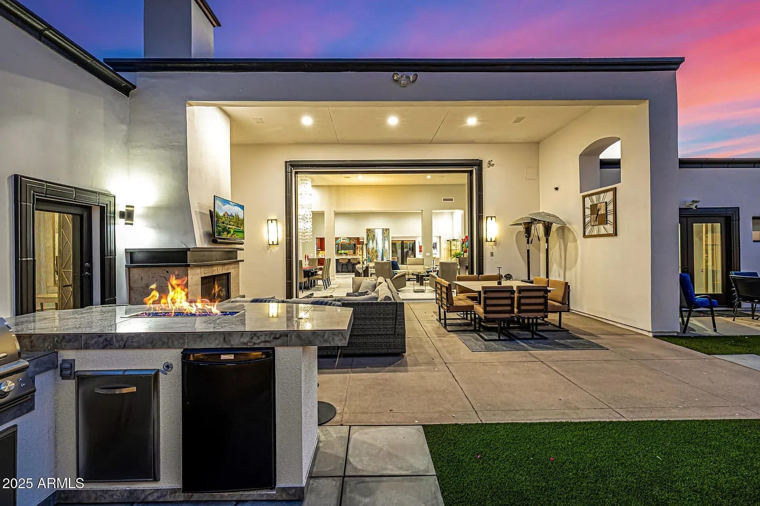 Outdoor patio with modern furniture, fire pit, and open indoor living area at sunset.