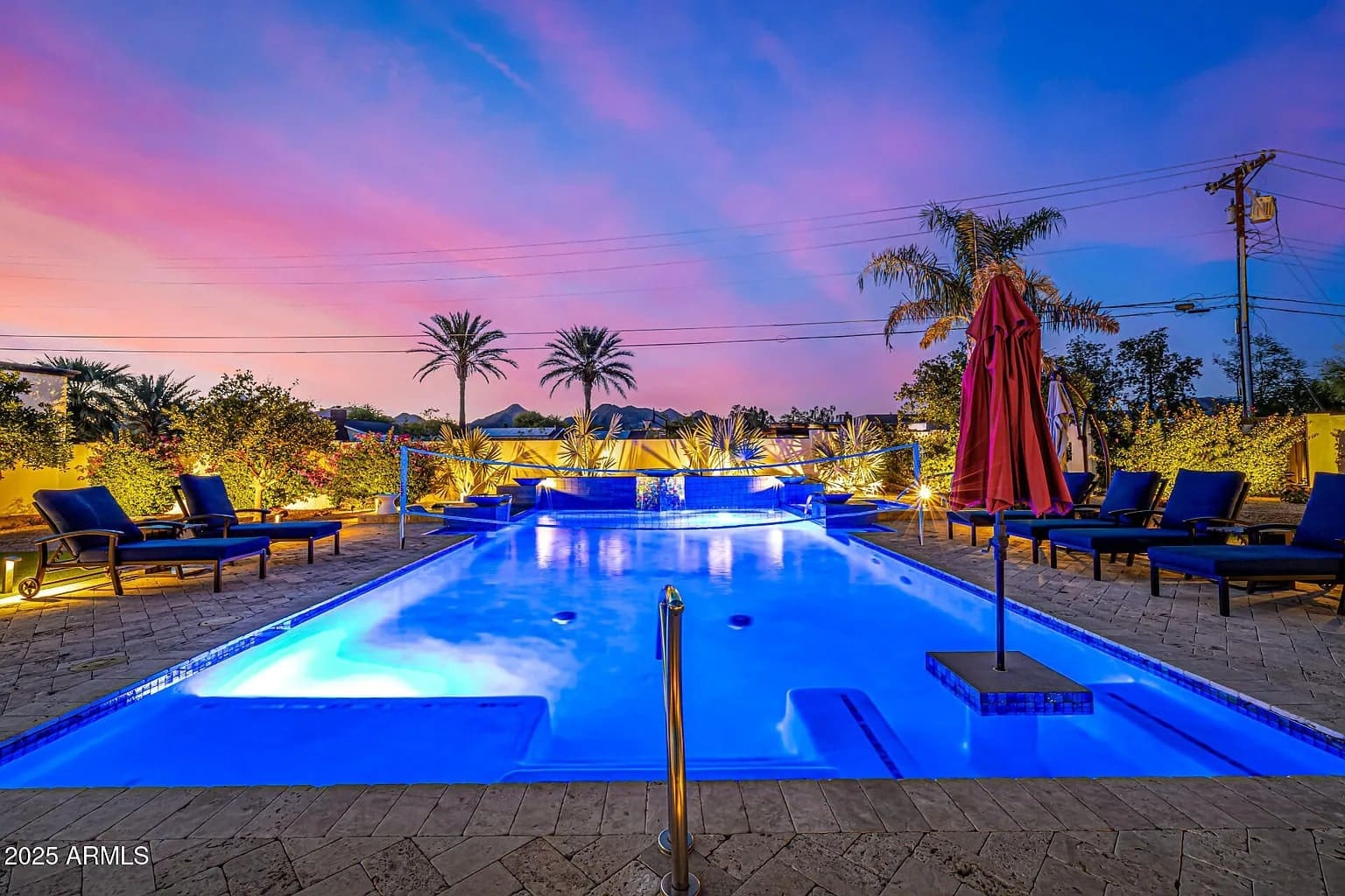 Outdoor pool area at sunset with lounge chairs, palm trees, and vibrant sky.