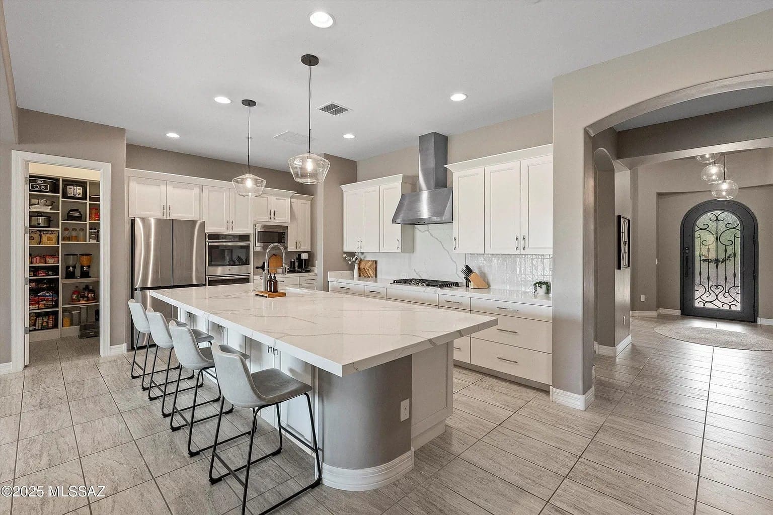 Modern kitchen with large island, bar stools, stainless steel appliances, and a walk-in pantry.