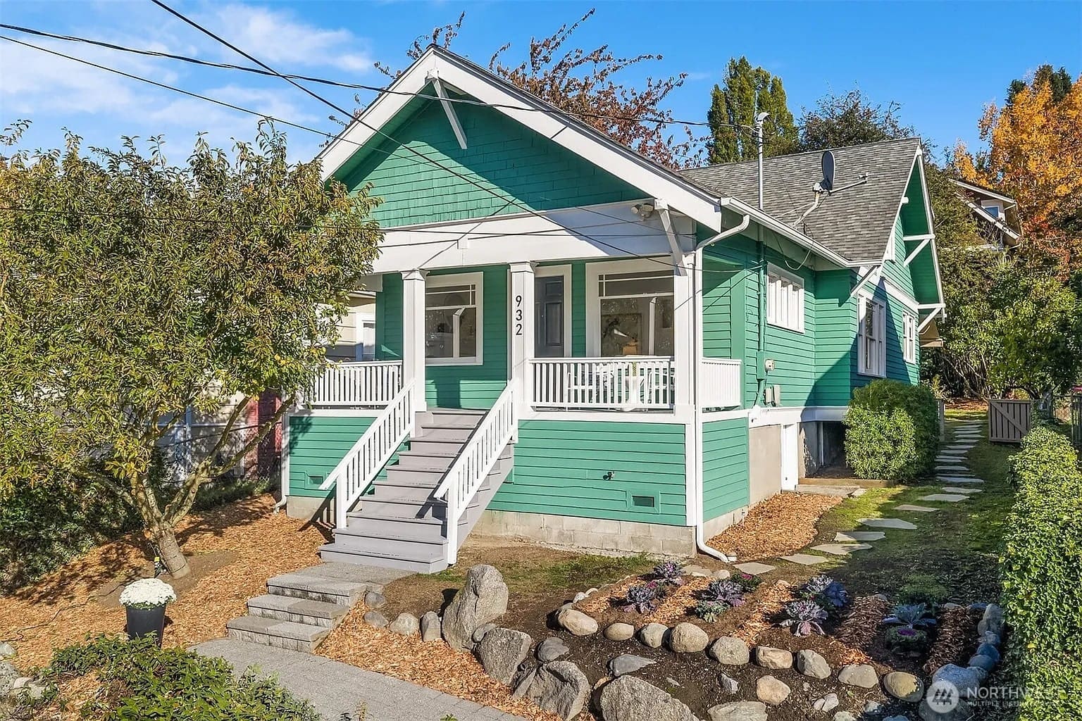 Green house with white trim, front porch, and landscaped yard with stone pathway and plants.