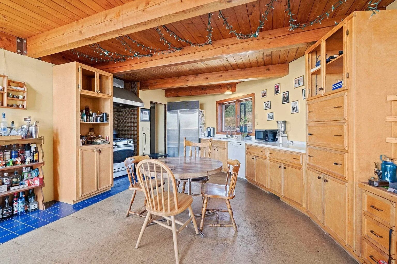 Spacious kitchen with wooden cabinets, round dining table, and appliances. Ceiling adorned with string lights.