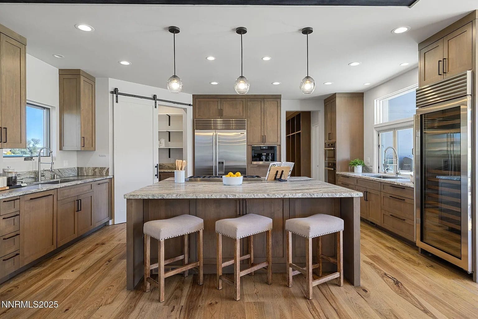 Modern kitchen with wooden cabinets, large island, bar stools, stainless steel appliances, and pendant lights.