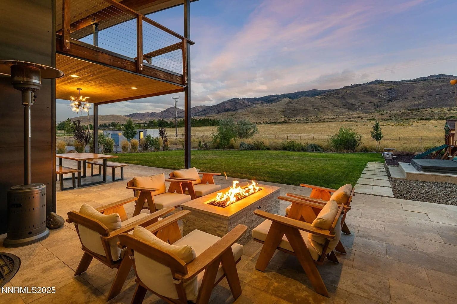 Patio with a fire pit, surrounded by chairs, overlooking a scenic mountain landscape at sunset.
