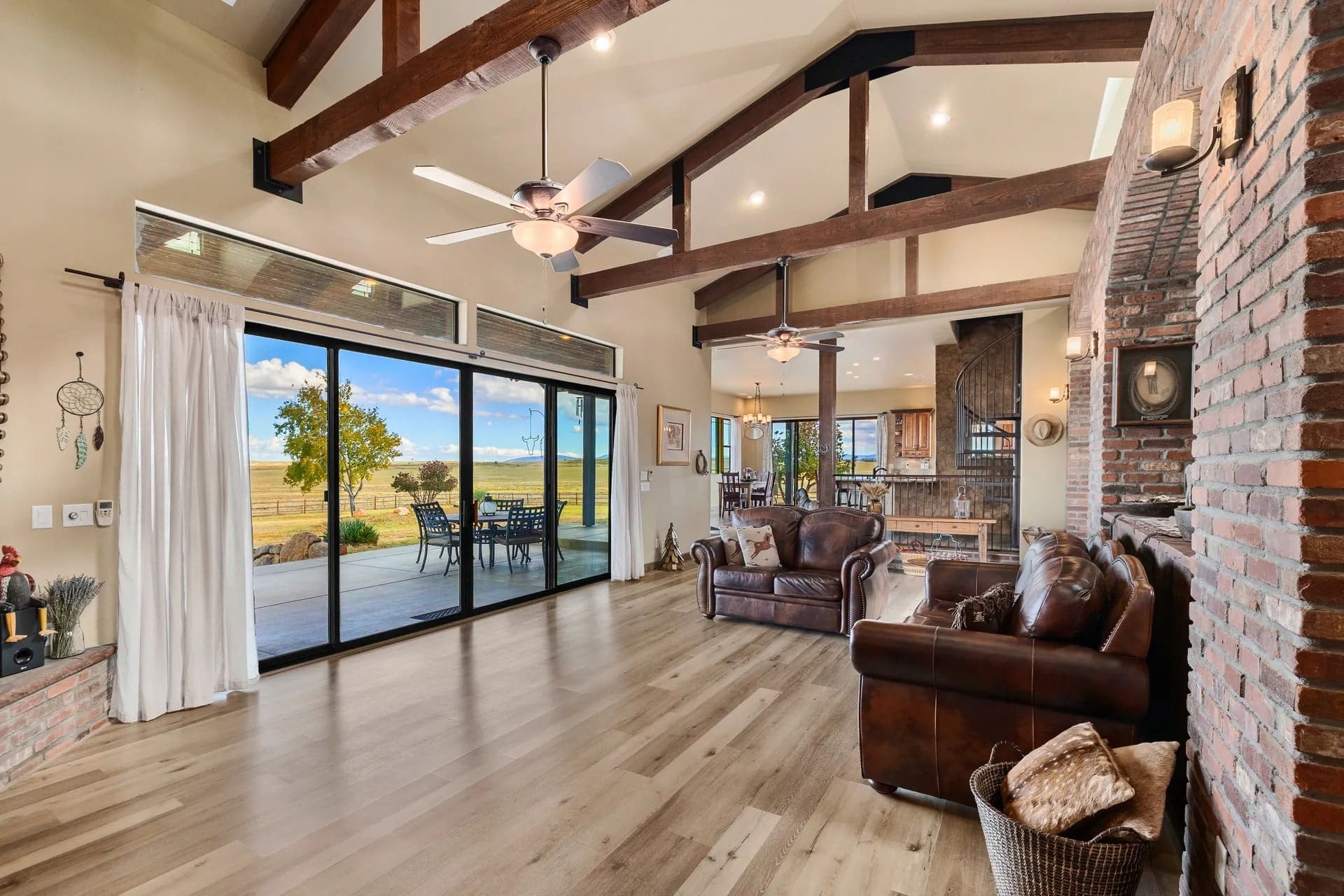 Spacious living room with leather sofas, wooden beams, and large sliding doors to a patio view.