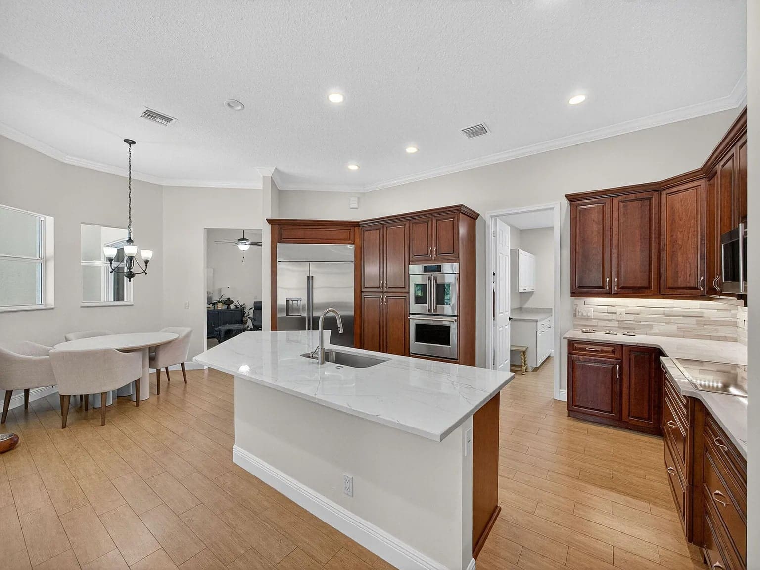 Modern kitchen with marble island, wooden cabinets, dining area, and stainless steel appliances.