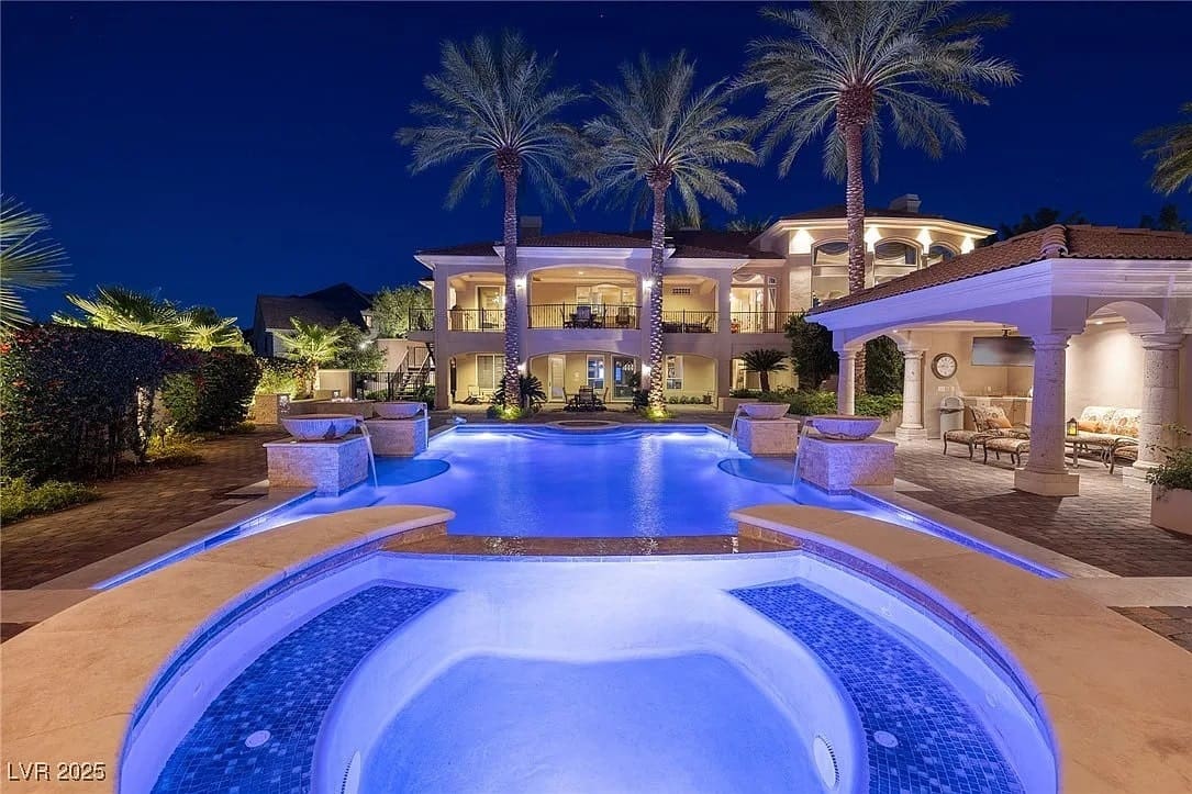 Luxurious mansion with illuminated pool and palm trees at night.