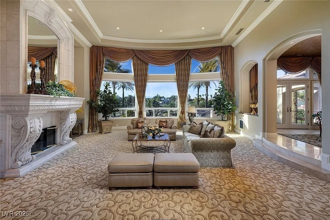 Luxurious living room with large windows, elegant furniture, ornate fireplace, and lush outdoor view.