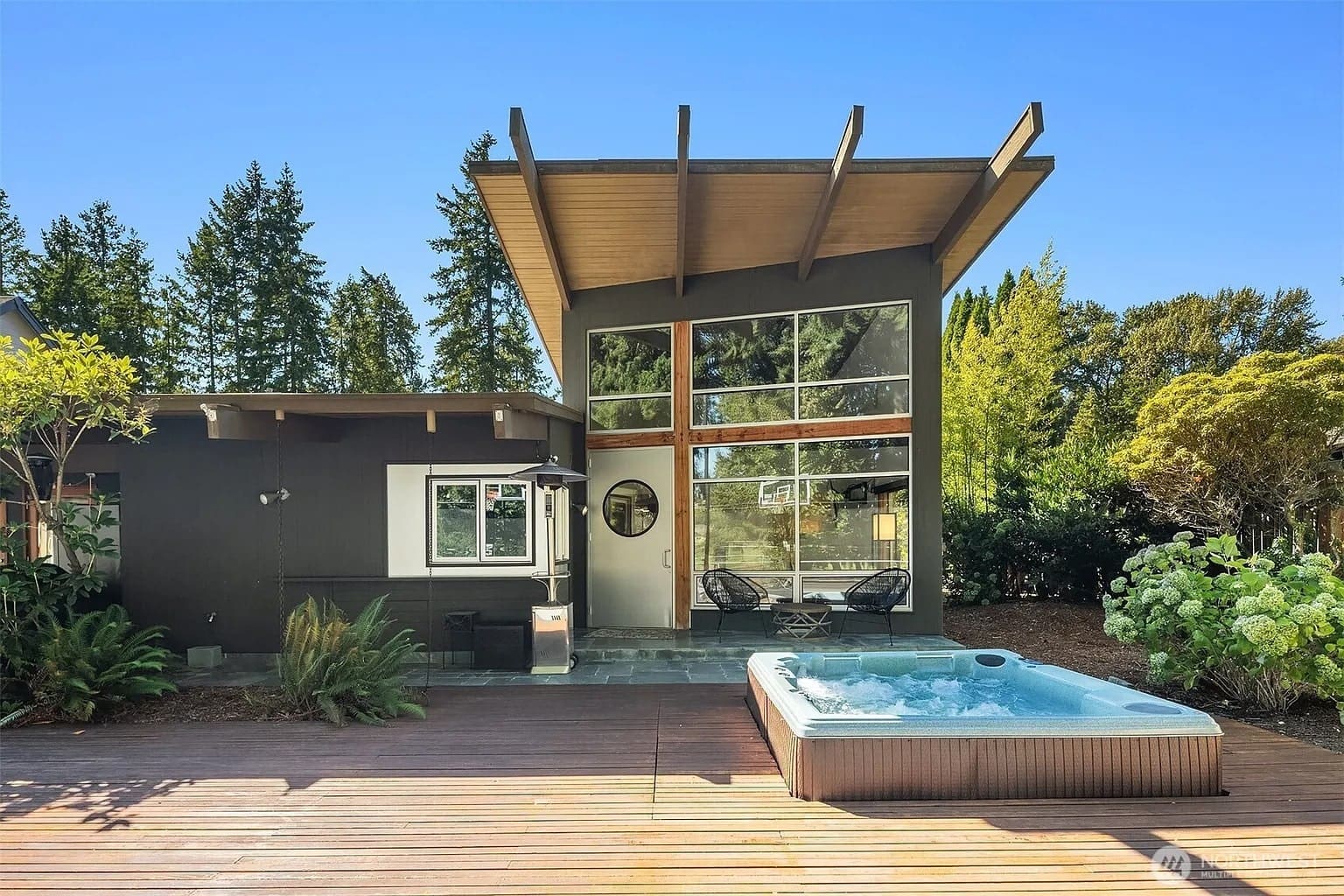 Modern house with large windows, patio, and outdoor hot tub surrounded by trees.