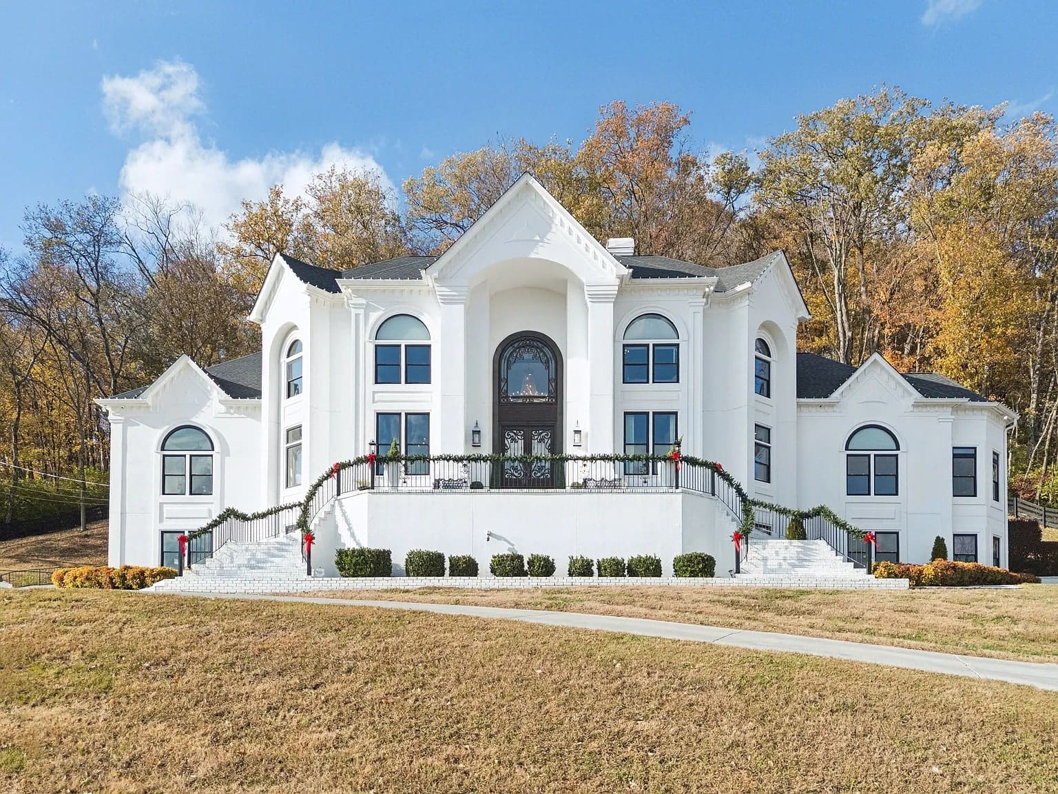 Large white mansion with arched windows, surrounded by autumn trees and a grassy lawn.