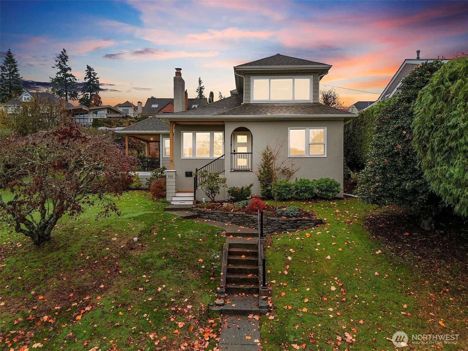 Two-story house with a front garden, surrounded by trees, at sunset.