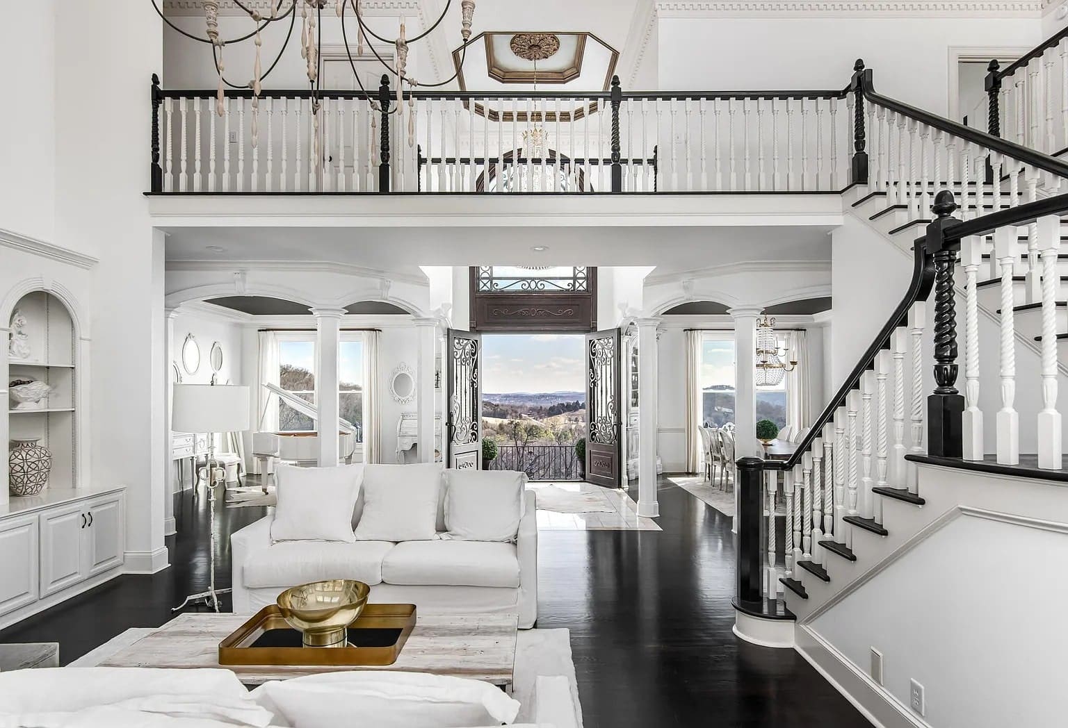 Spacious, elegant living room with white furniture, dark wood floors, and a view of the outdoors.