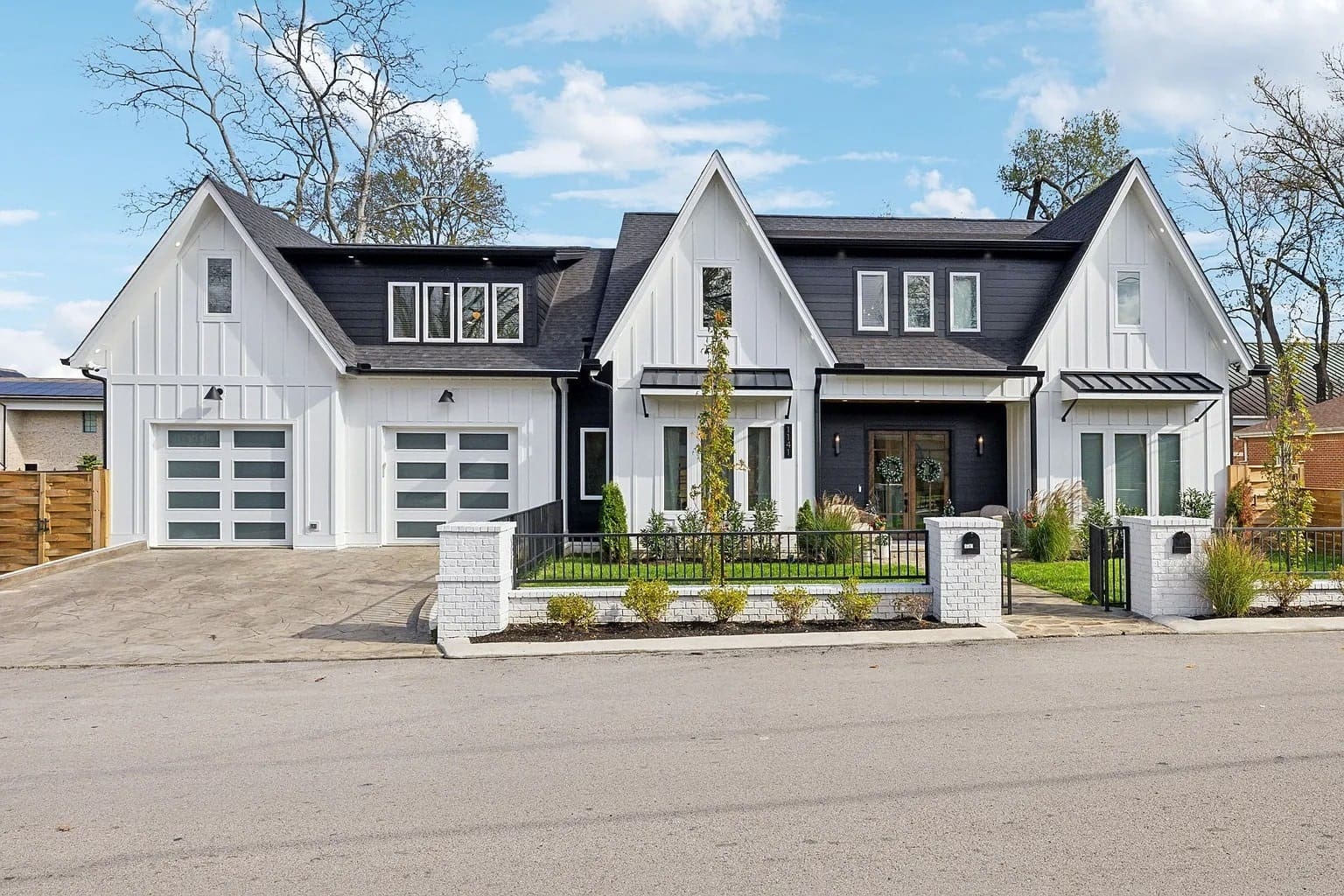 Modern white house with black roof, two garages, and a landscaped front yard.