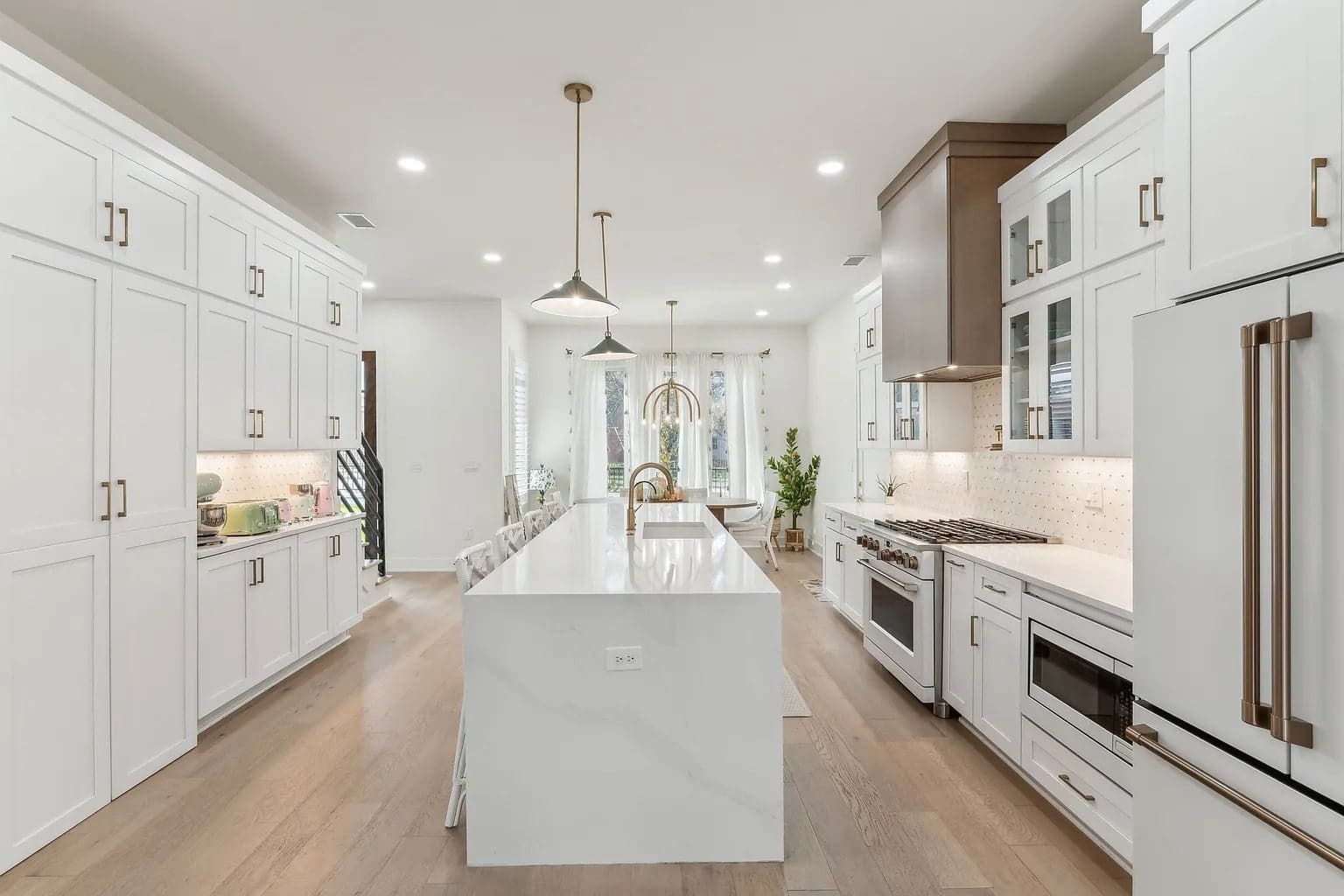 Modern kitchen with white cabinets, large island, pendant lights, and stainless steel appliances.