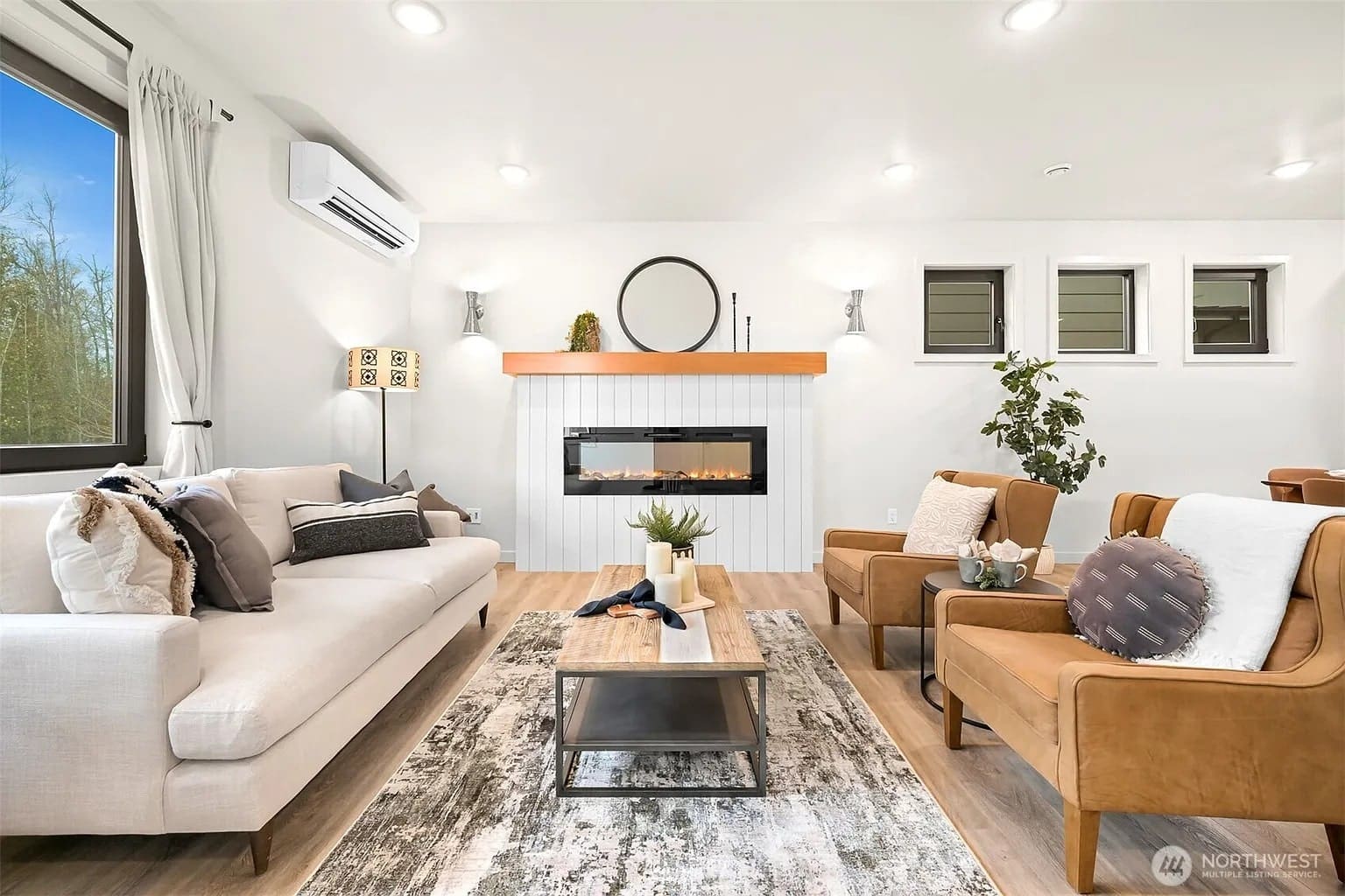 Modern living room with a beige sofa, armchairs, fireplace, and large window. Neutral decor accents.