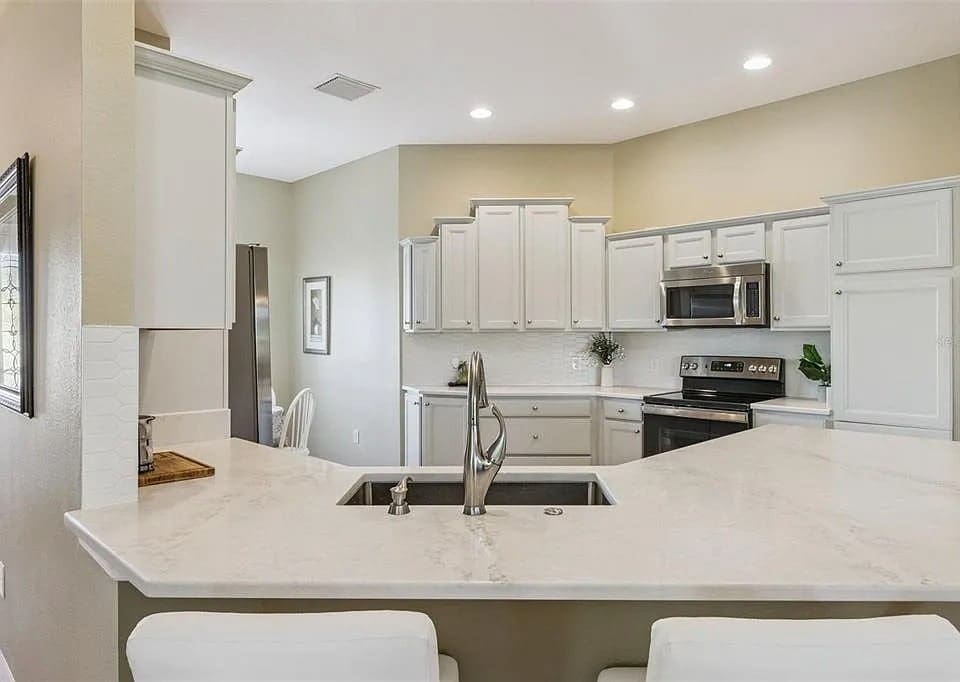 Modern kitchen with white cabinets, marble countertops, stainless steel appliances, and recessed lighting.